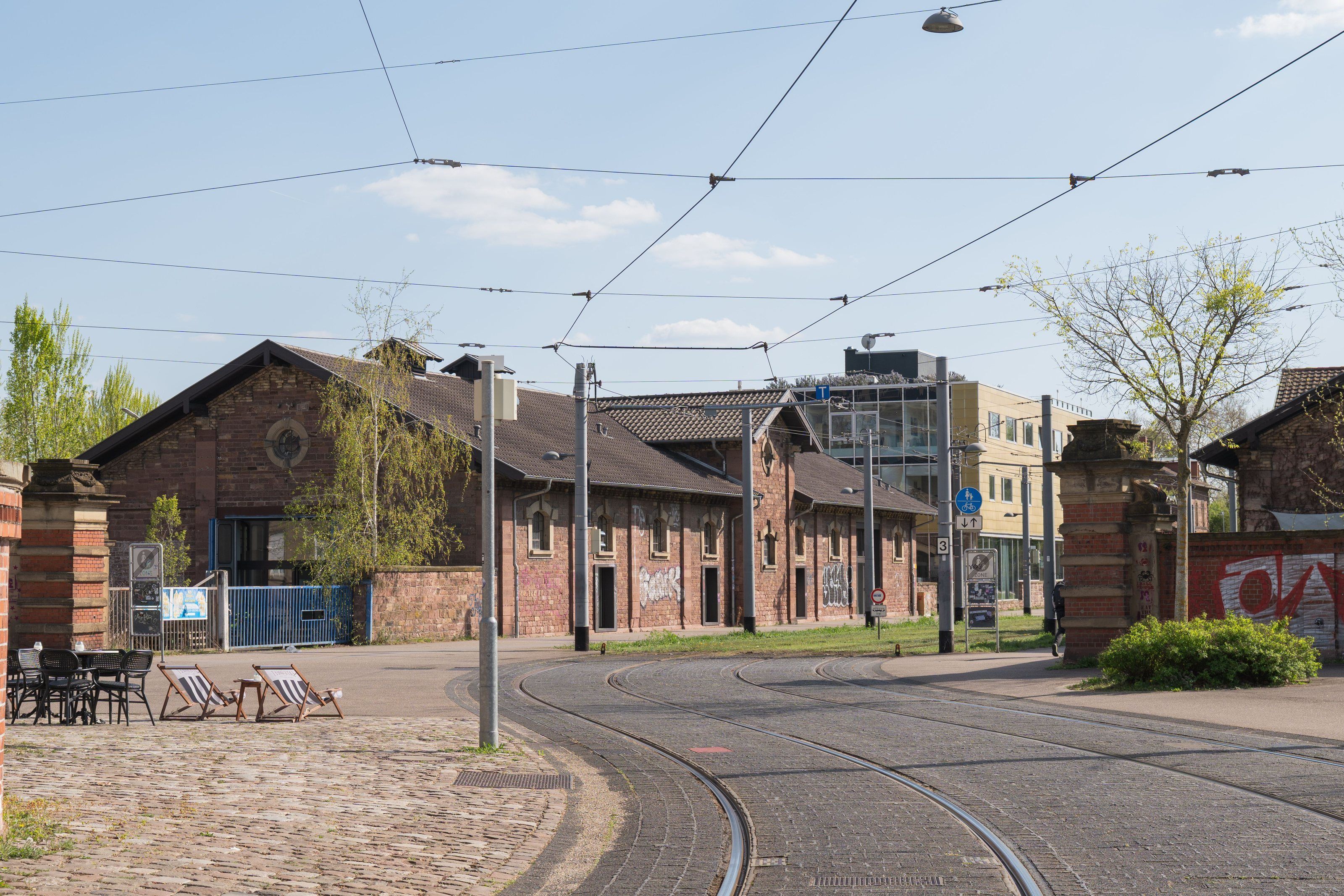 Straßenbahngleise bei Backsteinhallen mit Liegestühlen und Bäumen in Karlsruhe